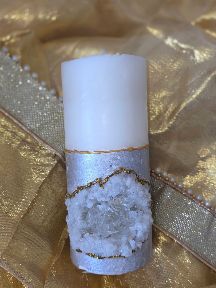 Pillar candle with druzzy texture, outlined with gold glitter, towards the bottom half, filled with Crystal glass. Top half is white coloured wax candle. Bottom half casted pillar with metallic grey shade.